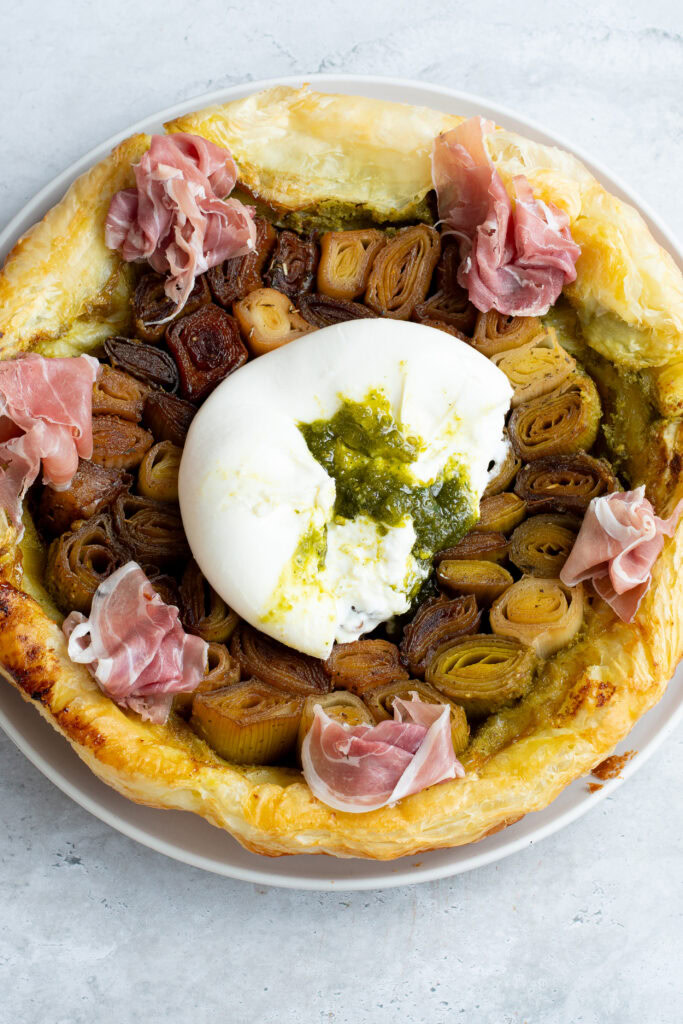 Tatin de poireaux sur une assiette avec une burrata fourrée au Pesto de pistache et du jambon de Parme.