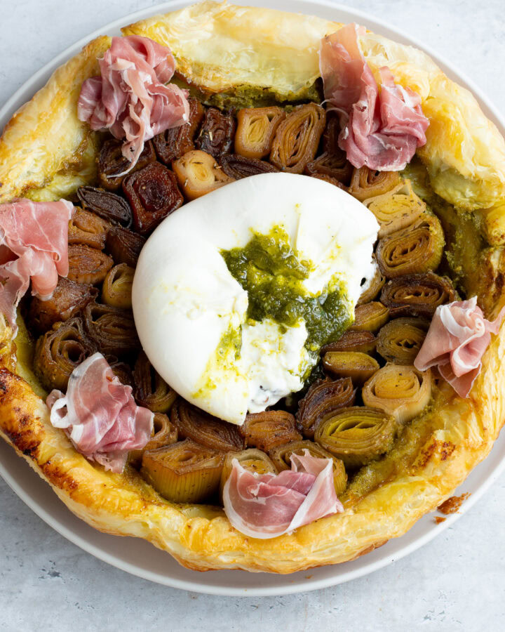 Leek tarte tatin on a plate with burrata stuffed with pistachio pesto and Parma ham.