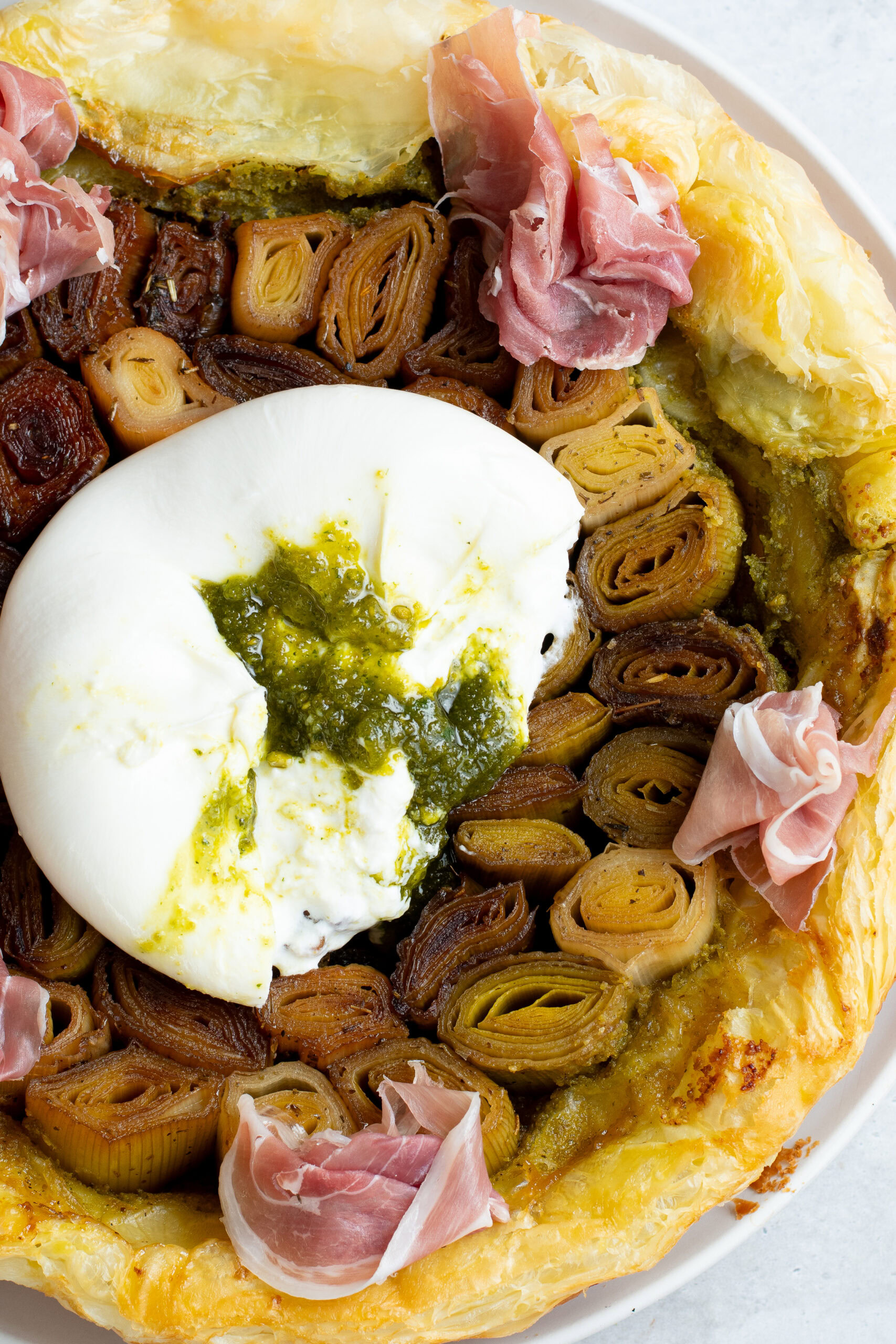 Leek tarte tatin on a plate with burrata stuffed with pistachio pesto and Parma ham.