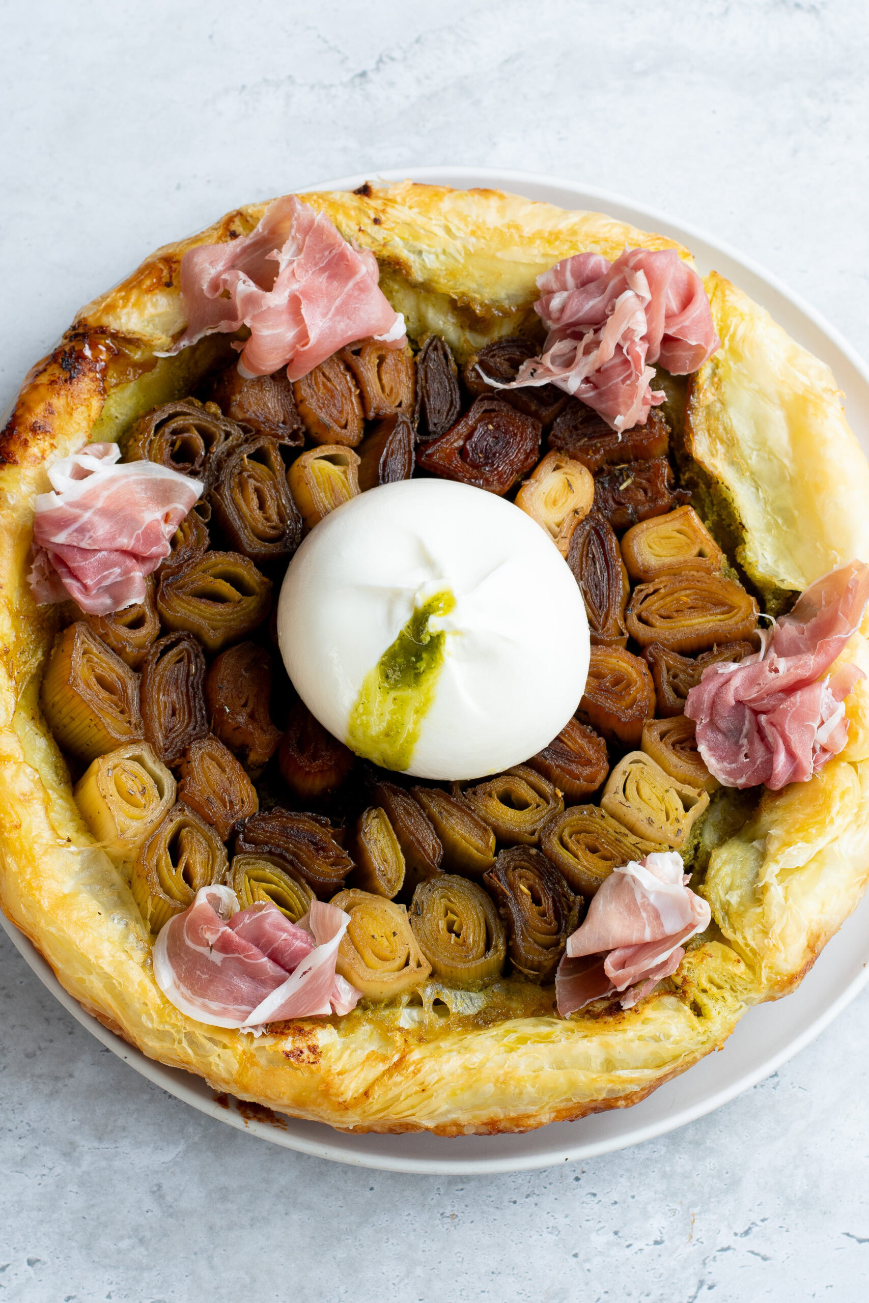 Leek tarte tatin on a plate with burrata stuffed with pistachio pesto and Parma ham.