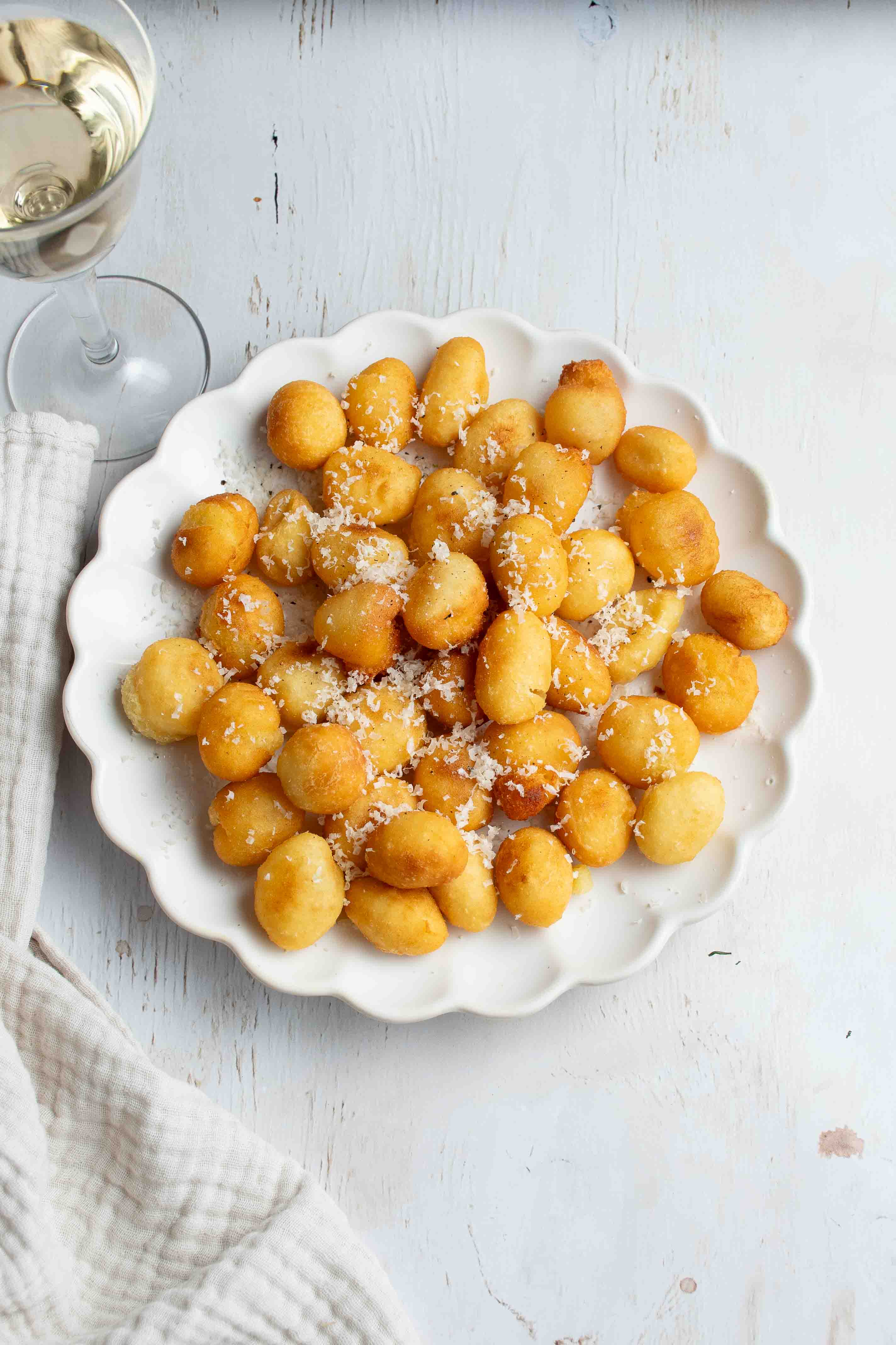 Gnocchi frits dans une assiette blanche et un verre de vin blanc.