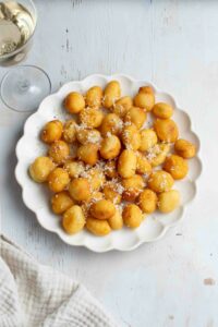 Gnocchi frits dans une assiette blanche et un verre de vin blanc.