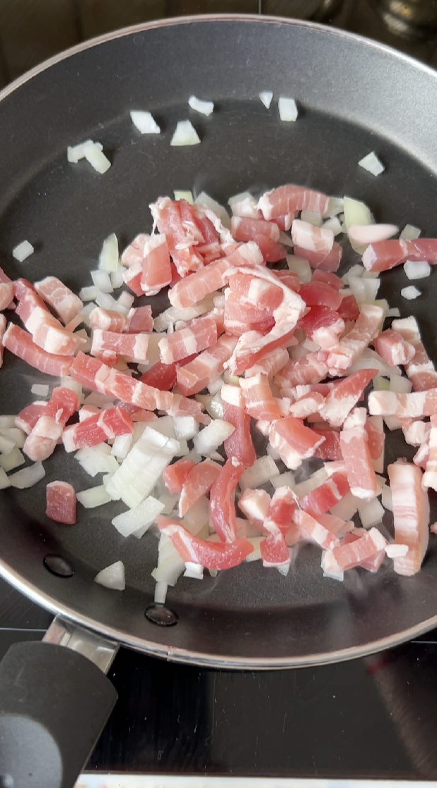 Oignon émincé et lardons qui cuisent dans une poêle.