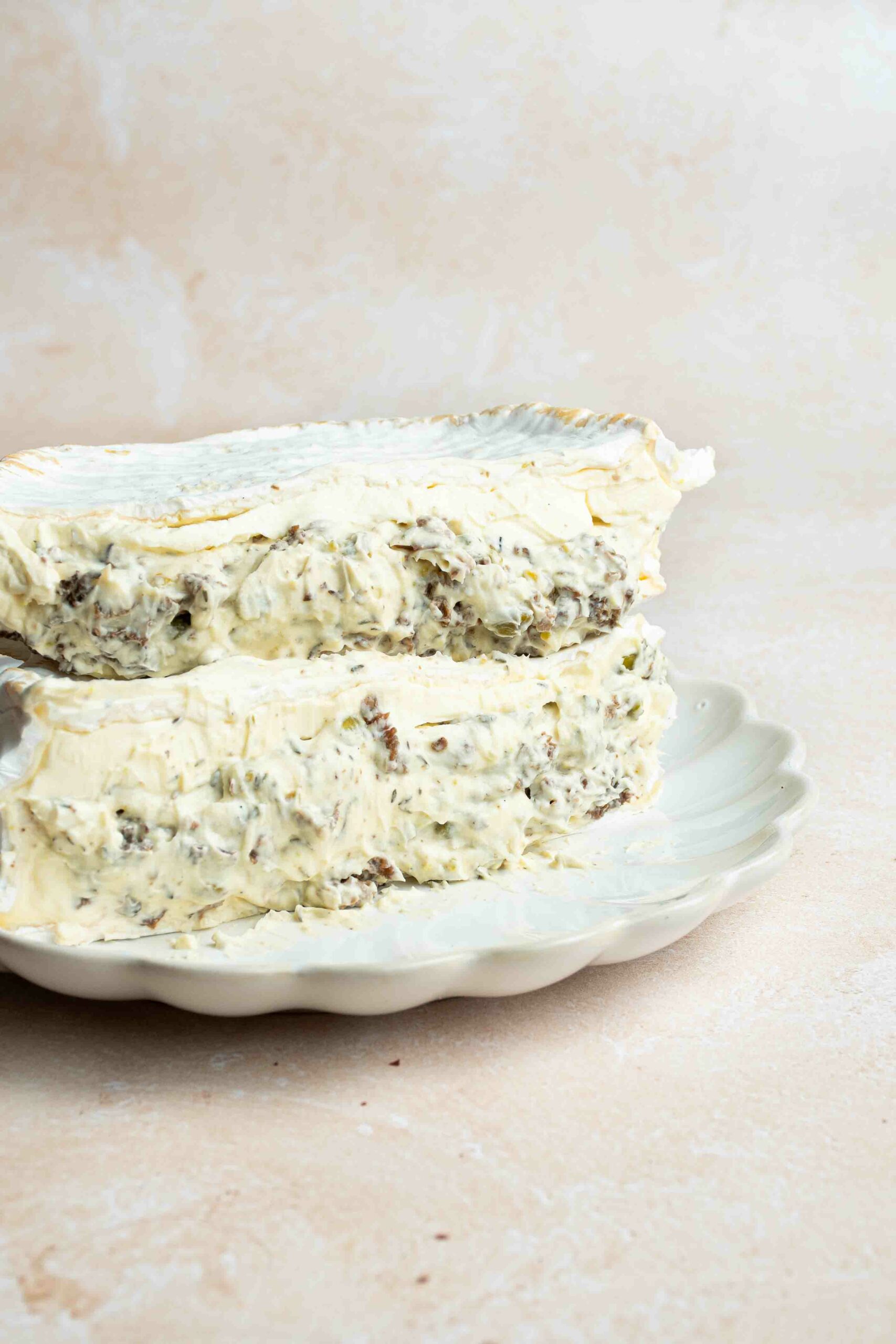 Deux moitiés de fromage maison garni de morilles, pistaches, thym et huile de truffe et empilées l'une sur l'autre dans une assiette blanche.