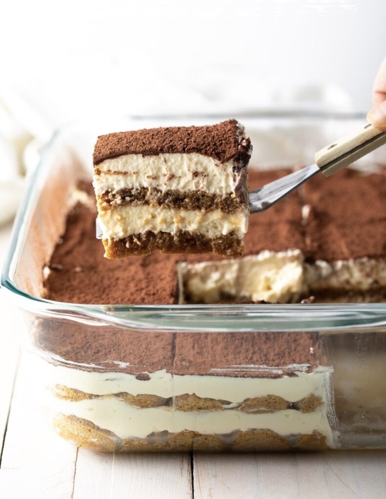 Une spatule qui sort une part de tiramisu du plat.