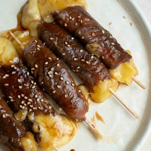 5 brochettes boeuf-fromage dans une assiette blanche avec des graines de sésame.