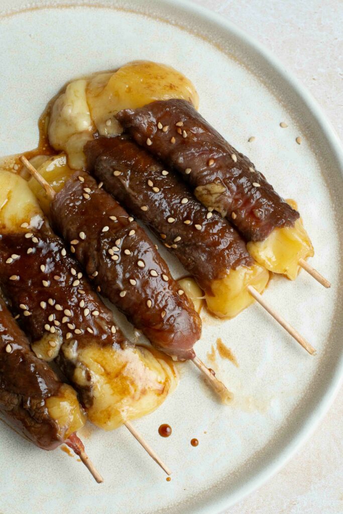 5 brochettes boeuf-fromage dans une assiette blanche avec des graines de sésame.