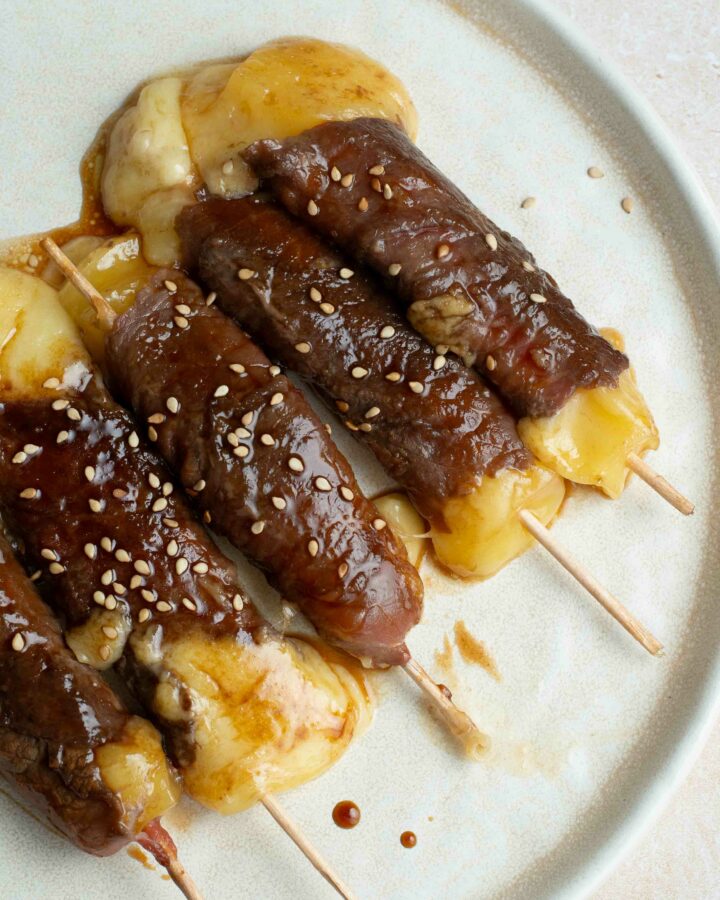 5 brochettes boeuf-fromage dans une assiette blanche avec des graines de sésame.