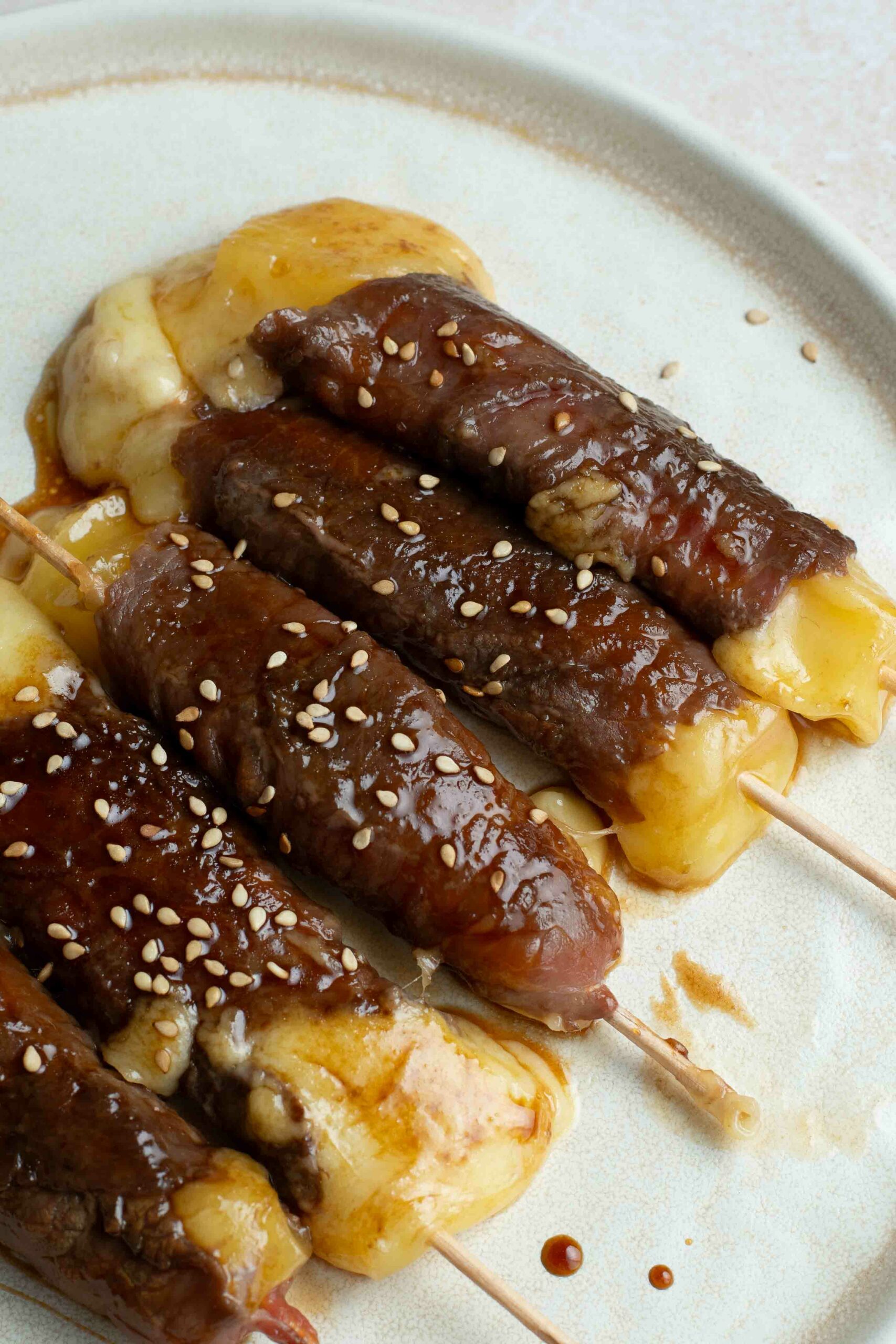 5 brochettes boeuf-fromage dans une assiette blanche avec des graines de sésame.