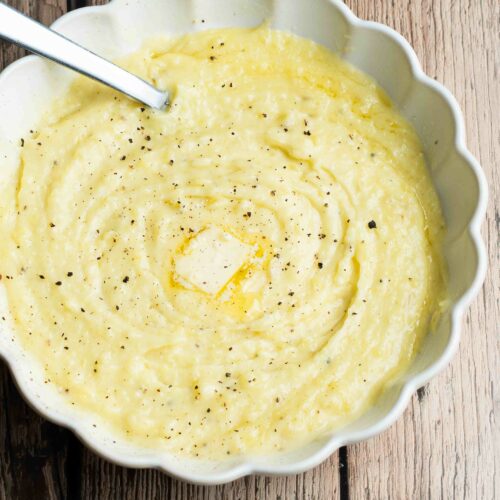 Purée de pommes de terre dans une assiette blanche ronde avec un petit carré de beurre, du poivre et une cuillère à soupe.