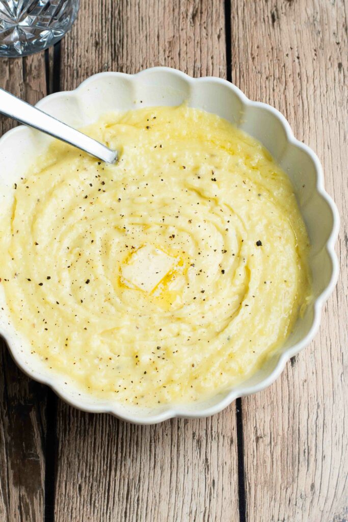 Purée de pommes de terre dans une assiette blanche ronde avec un petit carré de beurre, du poivre et une cuillère à soupe.