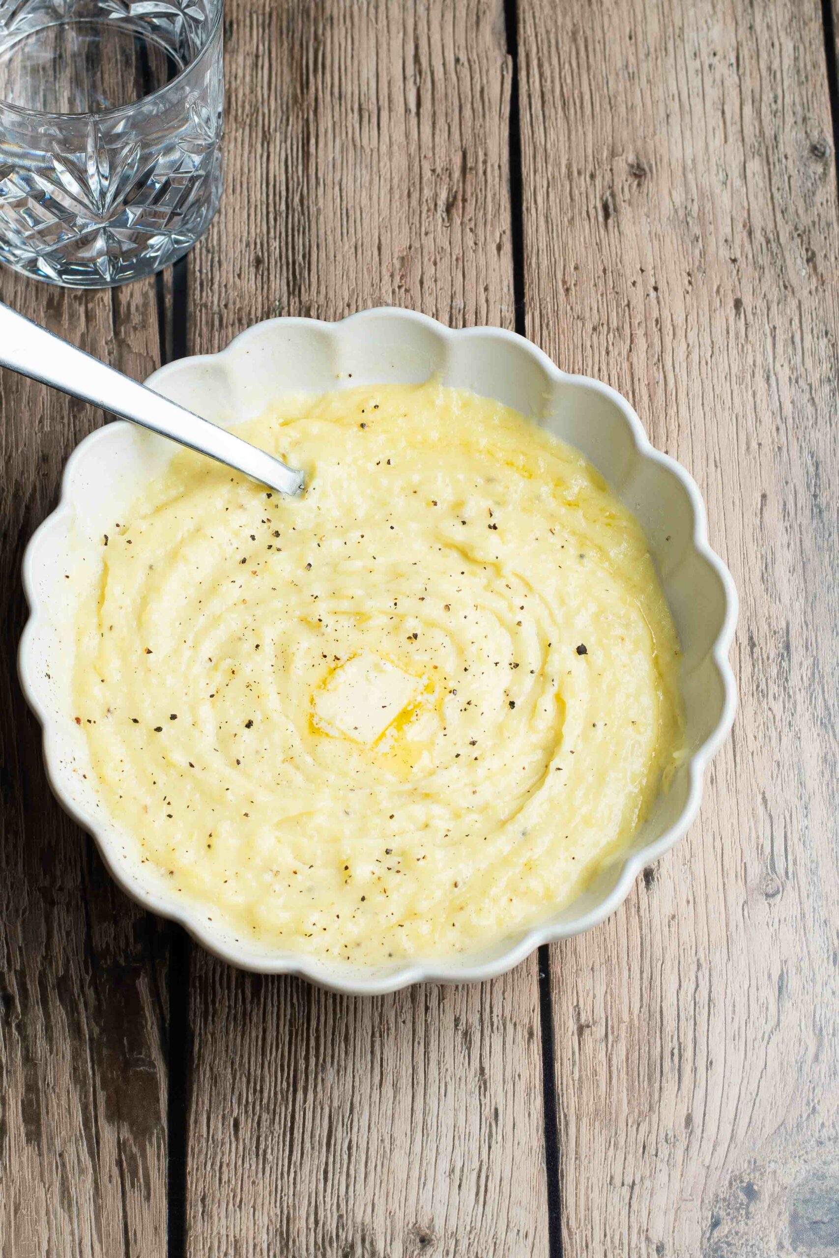 Purée de pommes de terre dans une assiette blanche ronde avec un petit carré de beurre, du poivre et une cuillère à soupe.