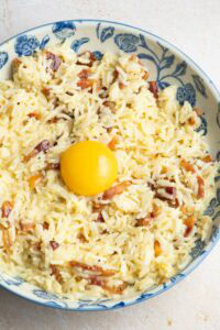 Riz Carbonara avec un jaune d'oeuf, dans une assiette beige et bleue.