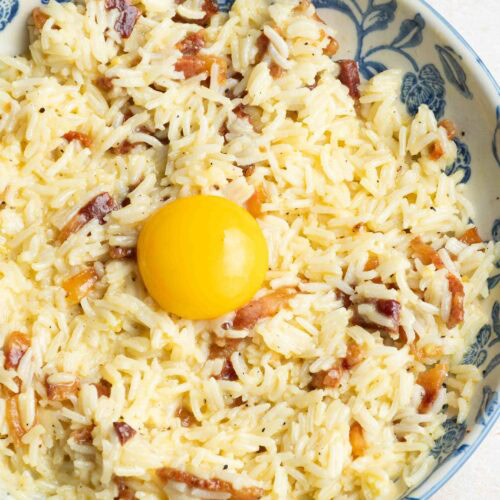 Riz Carbonara avec un jaune d'oeuf, dans une assiette beige et bleue.